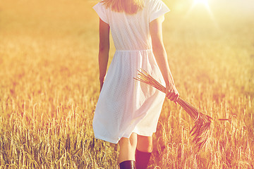 Image showing young woman with cereal spikelets walking on field