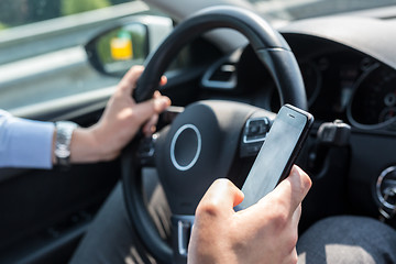 Image showing Businessman texting on his mobile phone while driving.