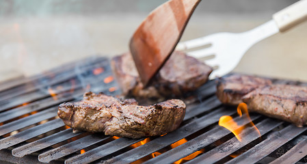 Image showing Chef grilling beef steaks on open flame BBQ.