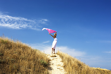 Image showing portrait of beautiful blond woman in white dress standing on wind with scarf near sea