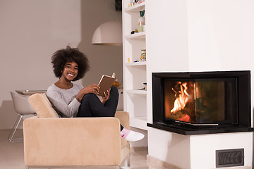 Image showing black woman reading book  in front of fireplace