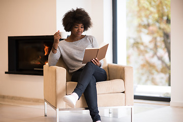 Image showing black woman reading book  in front of fireplace