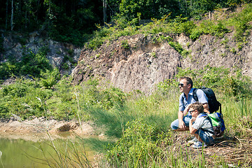 Image showing Father and son siting near the pond at the day time.