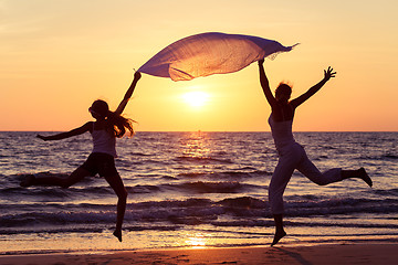 Image showing Mother and daughter jumping on the beach at the sunset time. 