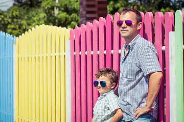 Image showing Father and son standing near the multicolored fence at the day t
