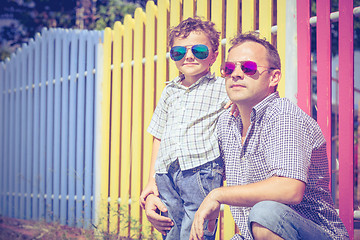 Image showing Father and son standing near the multicolored fence at the day t