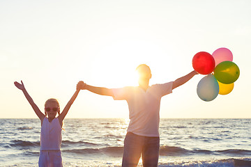 Image showing Father and daughter with balloons playing on the beach at the su