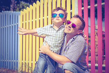 Image showing Father and son standing near the multicolored fence at the day t