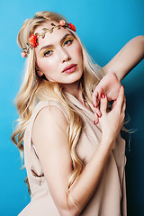 Image showing young pretty blond girl with curly blond hair and little lowers happy smiling on blue sky background, lifestyle people concept