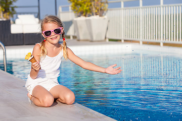 Image showing happy little girl with ice cream  sitting near a swimming pool