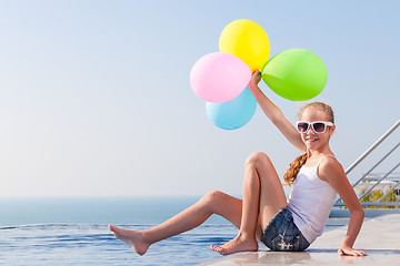 Image showing happy teen girl with balloons sitting near a swimming pool