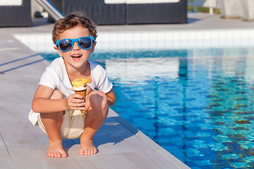 Image showing happy little boy with ice cream  sitting near a swimming pool