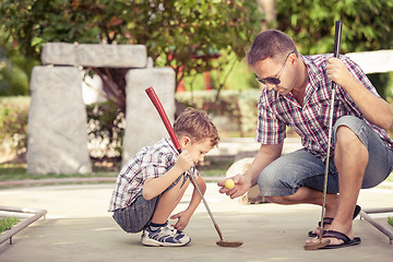 Image showing Cheerful young man teaching his son to play mini golf at the day