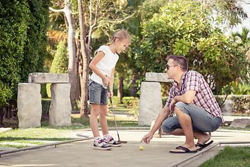 Image showing Cheerful young man teaching his daughter to play mini golf at th