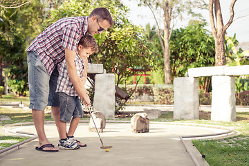 Image showing Cheerful young man teaching his son to play mini golf at the day