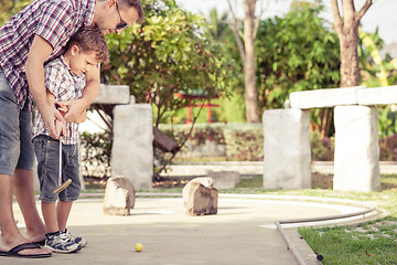 Image showing Cheerful young man teaching his son to play mini golf at the day