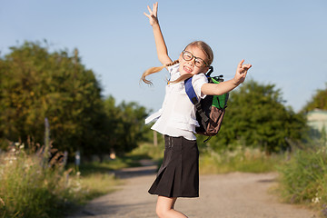 Image showing Smiling young school girl in a school uniform jumping on the roa