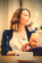 Image showing cup of tea on the table and a woman with a smartphone in the blu