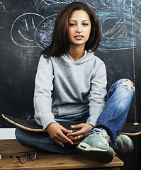 Image showing young cute teenage girl in classroom at blackboard seating on ta