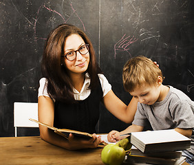 Image showing little cute boy with young teacher in classroom studying at blac