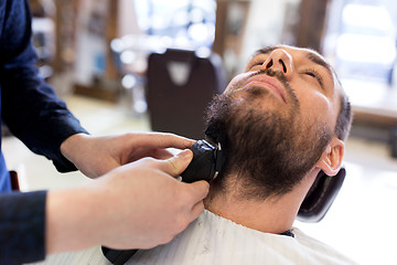 Image showing man and barber with trimmer cutting beard at salon