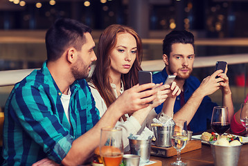 Image showing friends with smartphones dining at restaurant