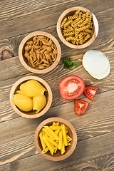 Image showing Variety of Pasta Wooden Bowls Cutting Boards Tomato Onion