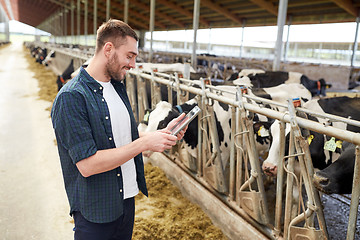 Image showing young man with tablet pc and cows on dairy farm