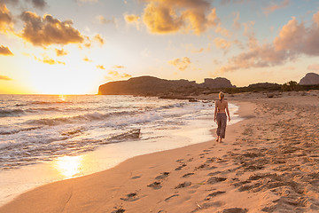 Image showing Woman walking on sandy beach at sunset.