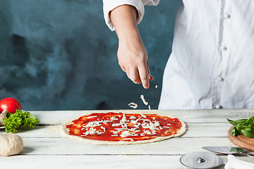 Image showing Closeup hand of chef baker in white uniform making pizza at kitchen