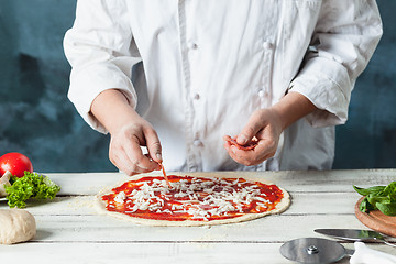 Image showing Closeup hand of chef baker in white uniform making pizza at kitchen