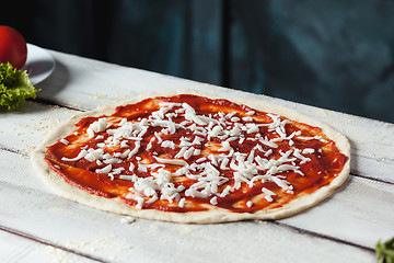 Image showing Closeup of a home made raw pizza with cheese and tomato sauce on a wooden background