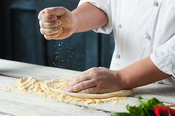 Image showing Closeup hand of chef baker in white uniform making pizza at kitchen