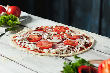 Image showing Closeup of a home made raw pizza with cheese and tomato sauce on a wooden background