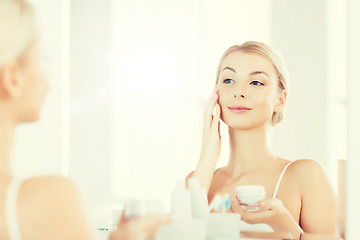 Image showing happy woman applying cream to face at bathroom