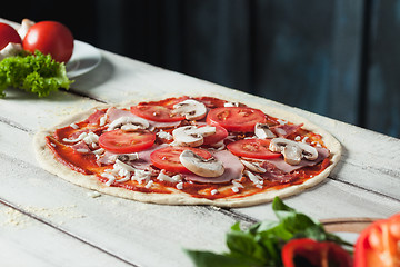 Image showing Closeup of a home made raw pizza with cheese and tomato sauce on a wooden background