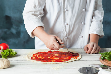 Image showing Closeup hand of chef baker in white uniform making pizza at kitchen