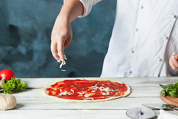 Image showing Closeup hand of chef baker in white uniform making pizza at kitchen