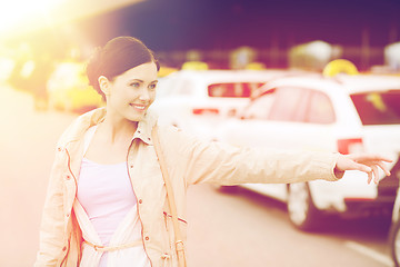 Image showing smiling young woman waving hand and catching taxi