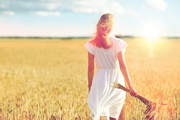 Image showing young woman with cereal spikelets walking on field