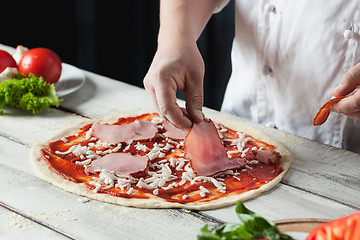 Image showing Closeup hand of chef baker in white uniform making pizza at kitchen