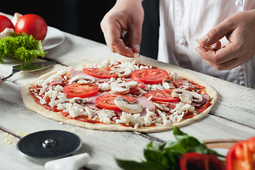 Image showing Closeup hand of chef baker in white uniform making pizza at kitchen