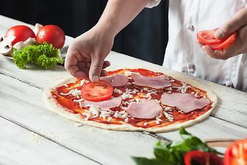 Image showing Closeup hand of chef baker in white uniform making pizza at kitchen