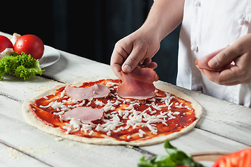 Image showing Closeup hand of chef baker in white uniform making pizza at kitchen