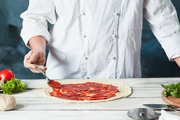 Image showing Closeup hand of chef baker in white uniform making pizza at kitchen