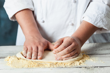 Image showing Closeup hand of chef baker in white uniform making pizza at kitchen