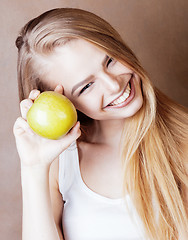 Image showing young pretty blond woman with green apple happy cheerful smiling close up on warm brown background, lifestyle real people concept