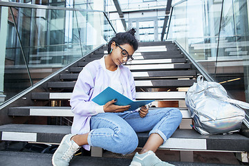 Image showing young cute indian girl at university building sitting on stairs reading a book, wearing hipster glasses, lifestyle people concept