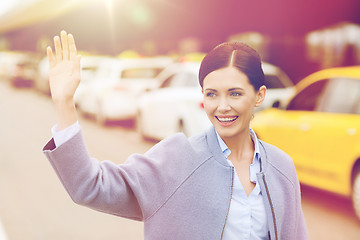 Image showing smiling young woman with waving hand over taxi