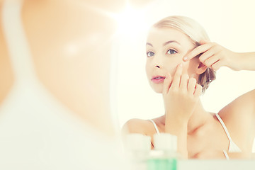 Image showing woman squeezing pimple at bathroom mirror